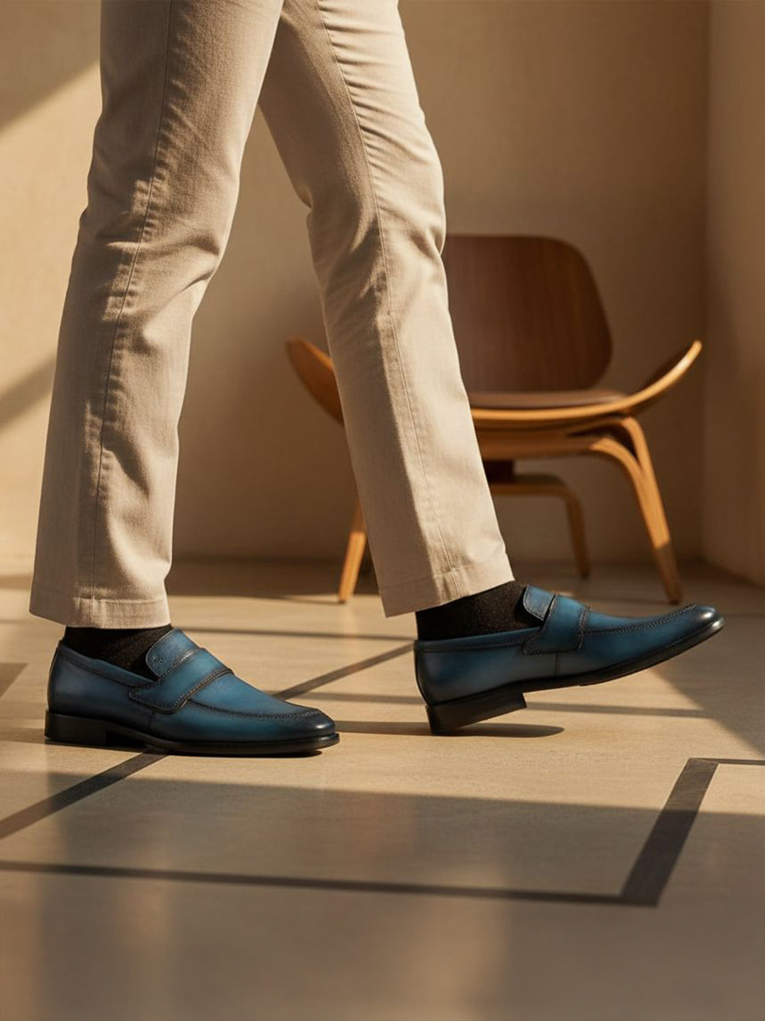 bugatti dark blue leather slip-on shoes with black socks and tan trousers, next to a wooden chair.

