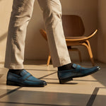 bugatti dark blue leather slip-on shoes with black socks and tan trousers, next to a wooden chair.
