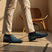 bugatti dark blue leather slip-on shoes with black socks and tan trousers, next to a wooden chair.
