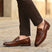 bugatti Mansueto cognac leather penny loafers with a textured strap detail, styled with brown trousers.
