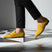 Yellow leather loafers by bugatti on black and white checkered flooring, paired with black trousers.