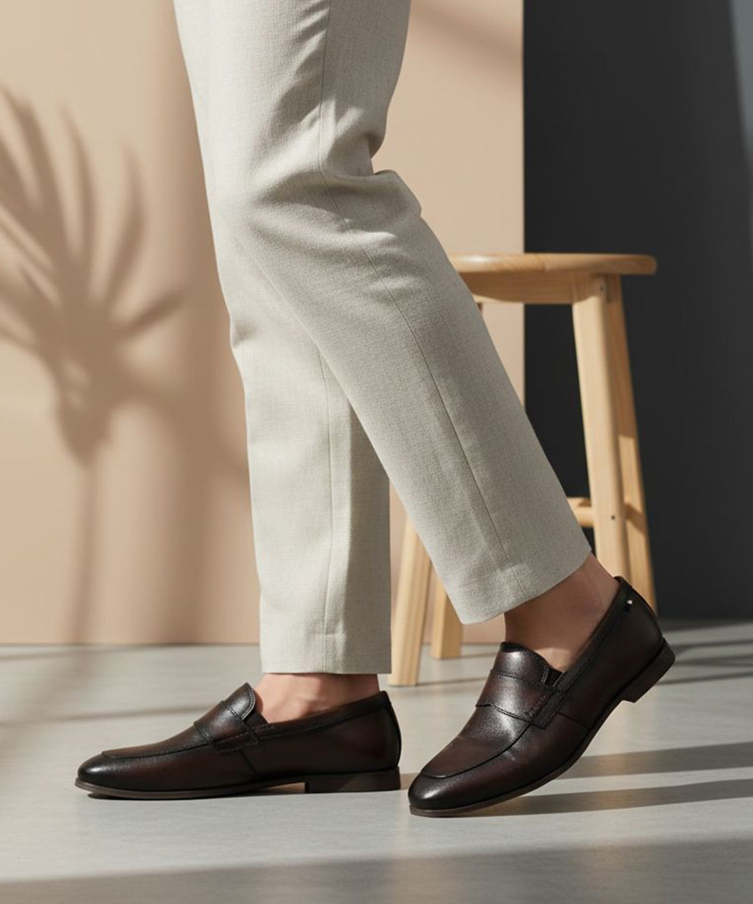 bugatti Tryst dark brown premium leather loafers with a classic penny strap, worn with beige pants.