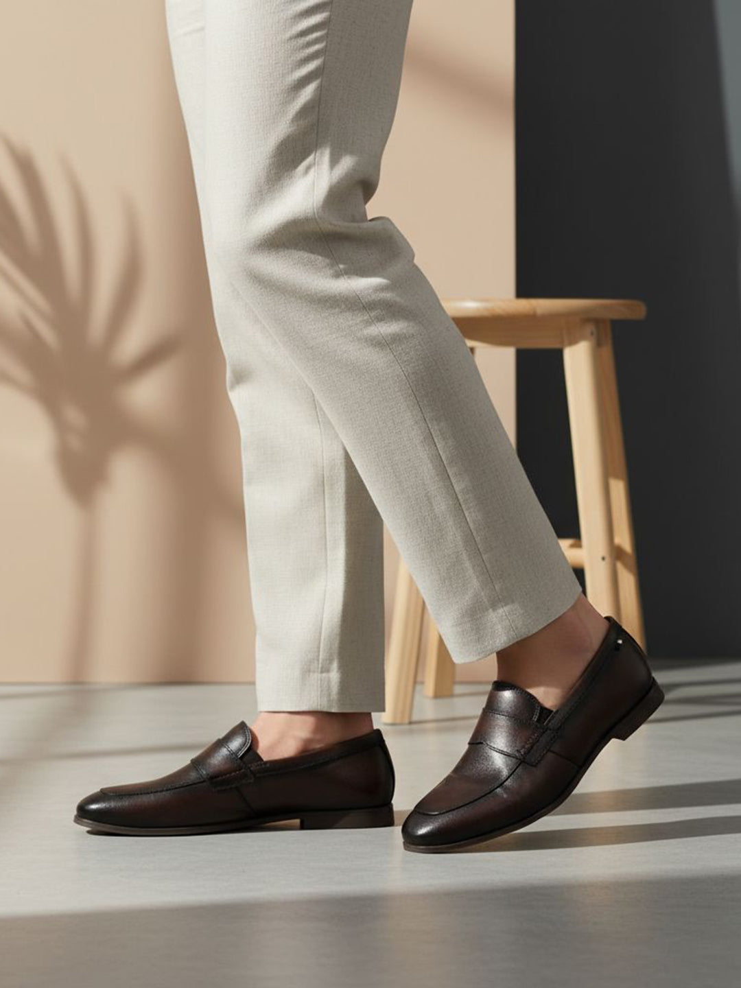 bugatti Tryst dark brown premium leather loafers with a classic penny strap, worn with beige pants.