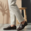 bugatti Tryst dark brown premium leather loafers with a classic penny strap, worn with beige pants.