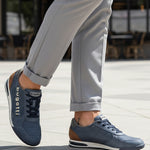 Lifestyle shot of bugatti Trevor blue Comfort Sneakers, a perforated leather shoe with brown heel detail, worn with gray slacks.
