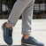 Lifestyle shot of bugatti Trevor blue Comfort Sneakers, a perforated leather shoe with brown heel detail, worn with gray slacks.
