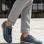 Lifestyle shot of bugatti Trevor blue Comfort Sneakers, a perforated leather shoe with brown heel detail, worn with gray slacks.
