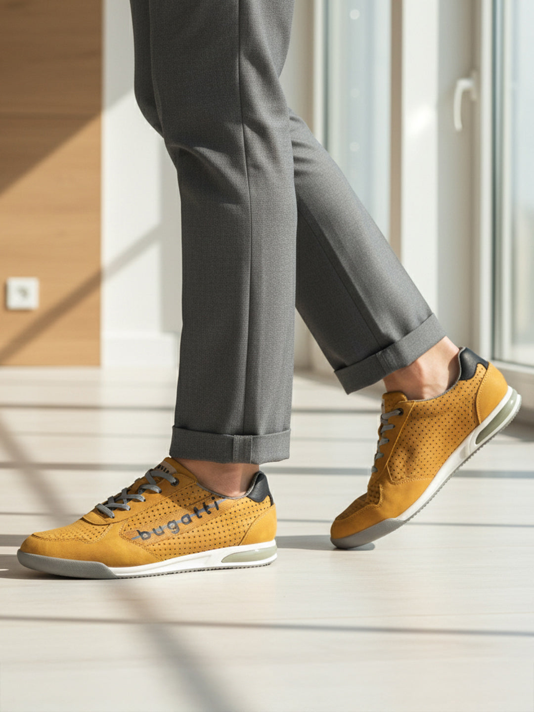 Lifestyle shot of bugatti Trevor yellow comfort sneakers, with grey laces, a perforated pattern, and grey dress pants.

