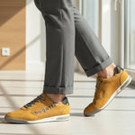 Lifestyle shot of bugatti Trevor yellow comfort sneakers, with grey laces, a perforated pattern, and grey dress pants.
