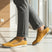 Lifestyle shot of bugatti Trevor yellow comfort sneakers, with grey laces, a perforated pattern, and grey dress pants.
