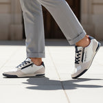 Lifestyle shot of bugatti Trevor white sneakers, with zipper detail, worn with gray pants and walking on pavement.