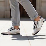Lifestyle shot of bugatti Trevor white sneakers, with zipper detail, worn with gray pants and walking on pavement.