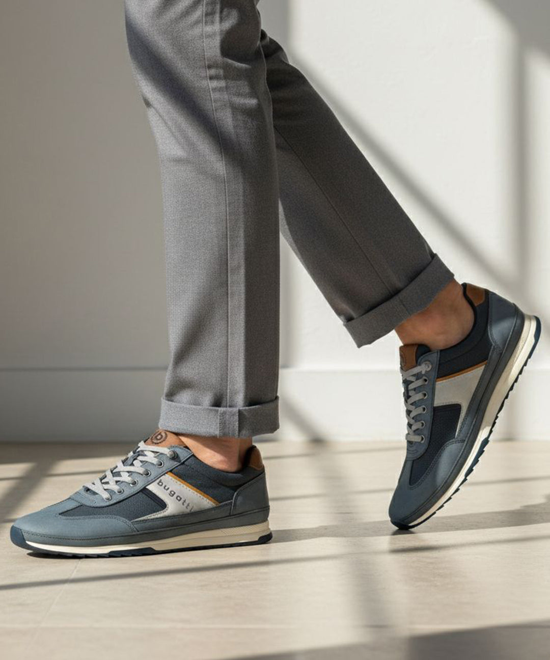 Lifestyle shot of bugatti Riptide blue comfort sneakers paired with gray dress pants and a cuffed hem.