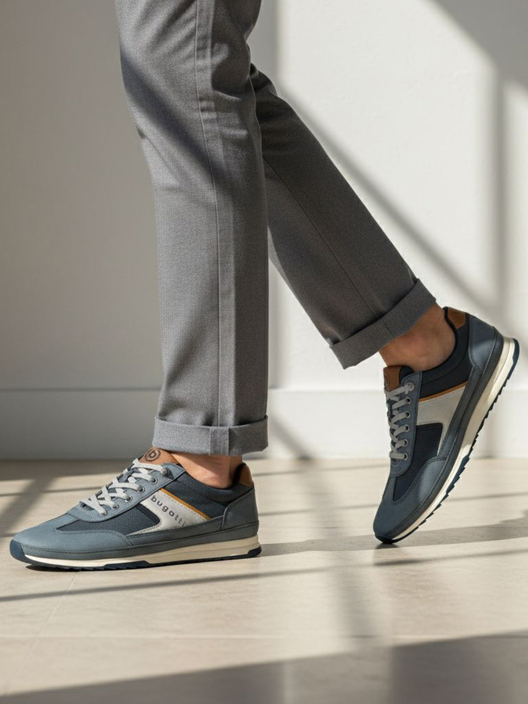 Lifestyle shot of bugatti Riptide blue comfort sneakers paired with gray dress pants and a cuffed hem.