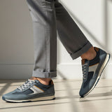 Lifestyle shot of bugatti Riptide blue comfort sneakers paired with gray dress pants and a cuffed hem.