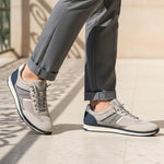Lifestyle image of bugatti Riptide sand Comfort Sneakers, with gray mesh and suede upper, dark blue accents, paired with gray trousers.
