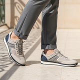 Lifestyle image of bugatti Riptide sand Comfort Sneakers, with gray mesh and suede upper, dark blue accents, paired with gray trousers.
