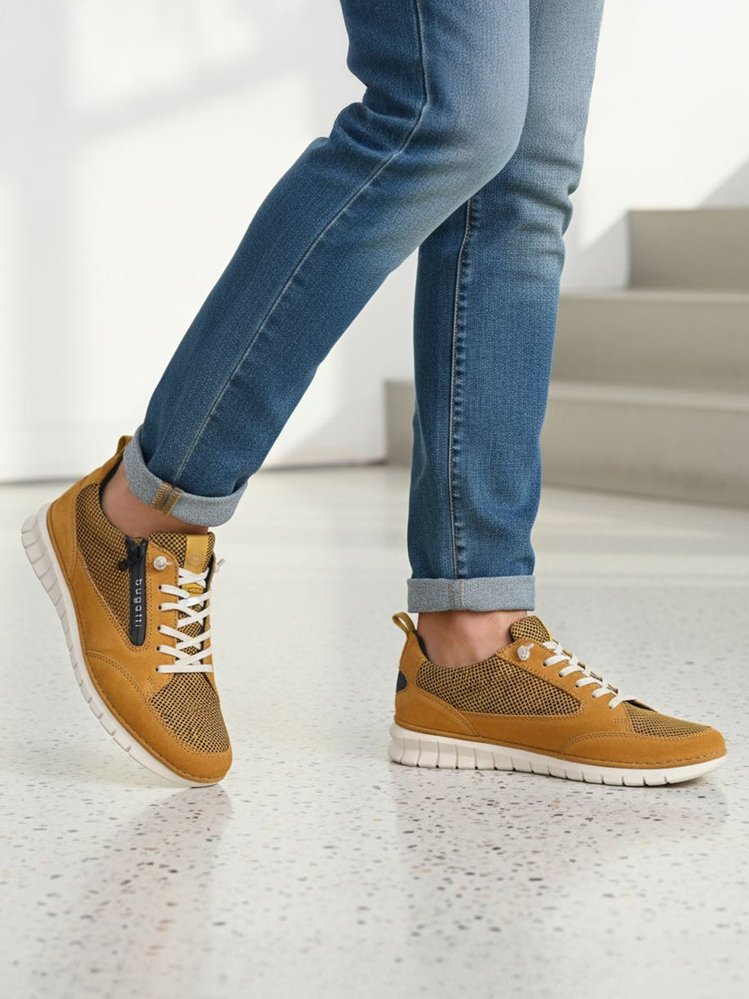 Lifestyle shot of bugatti Palenque yellow leather sneakers with white soles, worn with blue jeans.
