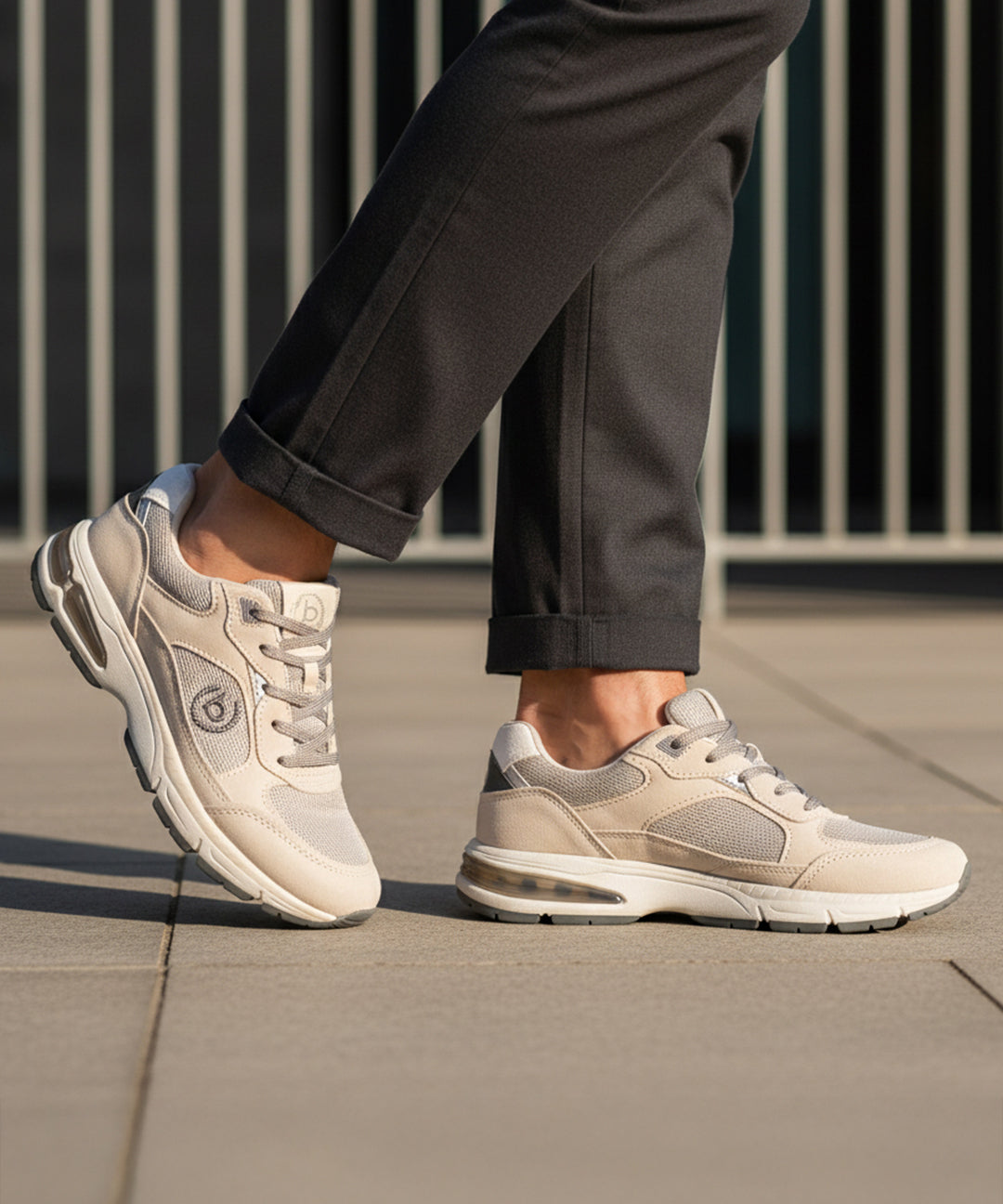 Lifestyle shot of bugatti Parry beige premium leather sneakers with gray mesh and rubber soles, worn with gray slacks.
