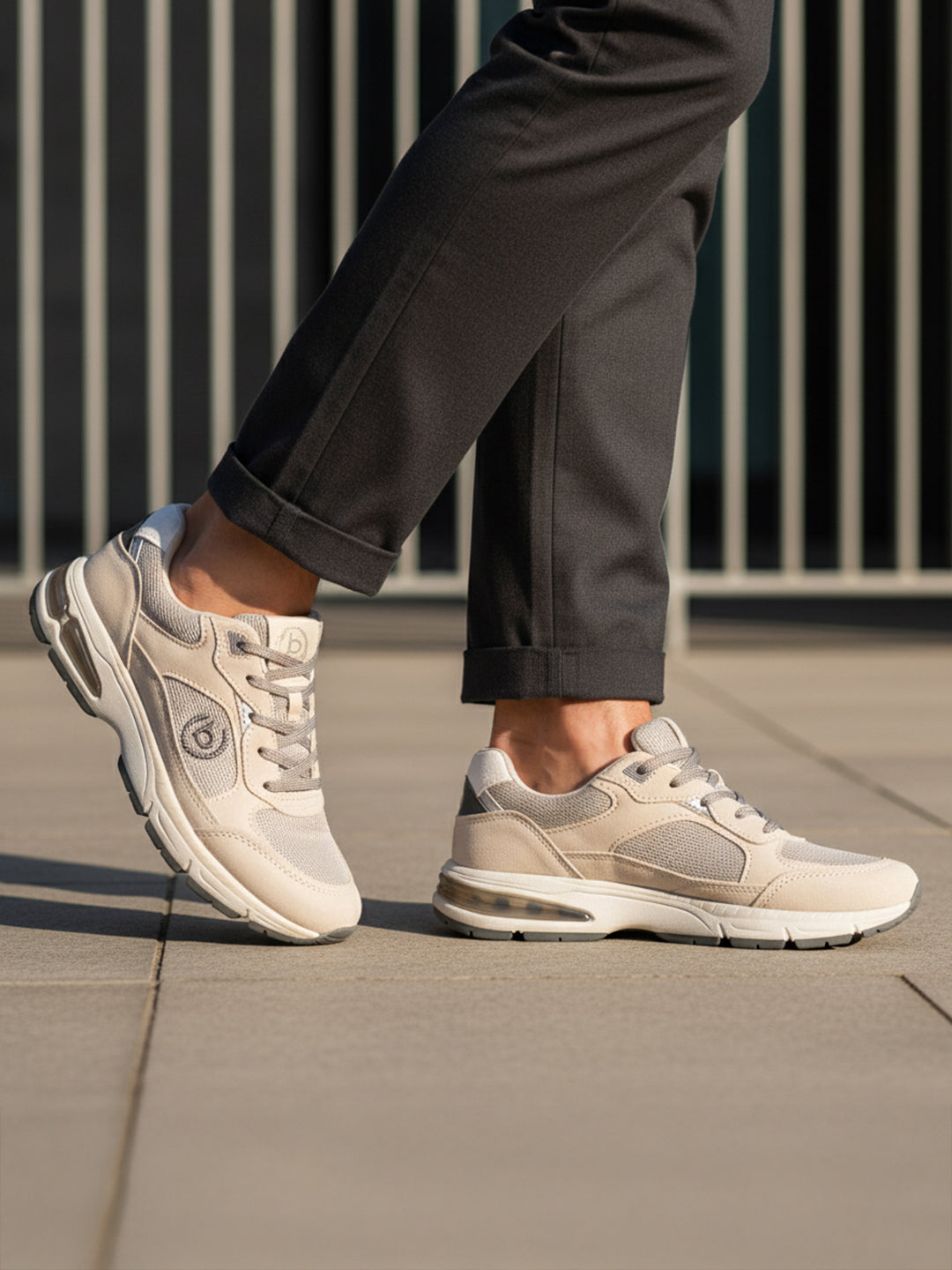 Lifestyle shot of bugatti Parry beige premium leather sneakers with gray mesh and rubber soles, worn with gray slacks.
