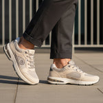 Lifestyle shot of bugatti Parry beige premium leather sneakers with gray mesh and rubber soles, worn with gray slacks.
