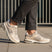 Lifestyle shot of bugatti Parry beige premium leather sneakers with gray mesh and rubber soles, worn with gray slacks.
