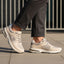 Lifestyle shot of bugatti Parry beige premium leather sneakers with gray mesh and rubber soles, worn with gray slacks.
