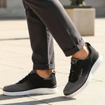 Lifestyle image of bugatti Astra athleisure sneakers in dark grey with a white sole, worn with rolled grey pants.
