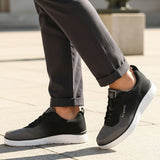 Lifestyle image of bugatti Astra athleisure sneakers in dark grey with a white sole, worn with rolled grey pants.

