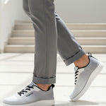 Lifestyle shot of bugatti Astra athleisure sneakers in white with black laces, paired with grey pants.
