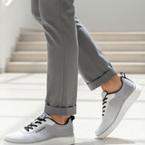 Lifestyle shot of bugatti Astra athleisure sneakers in white with black laces, paired with grey pants.
