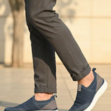 bugatti Astra blue slip-on casual shoes with a knit texture and white soles, styled with gray trousers.
