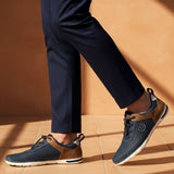 Lifestyle close-up of bugatti Glenans dark blue comfort sneakers with brown accents and white soles, paired with navy dress pants.