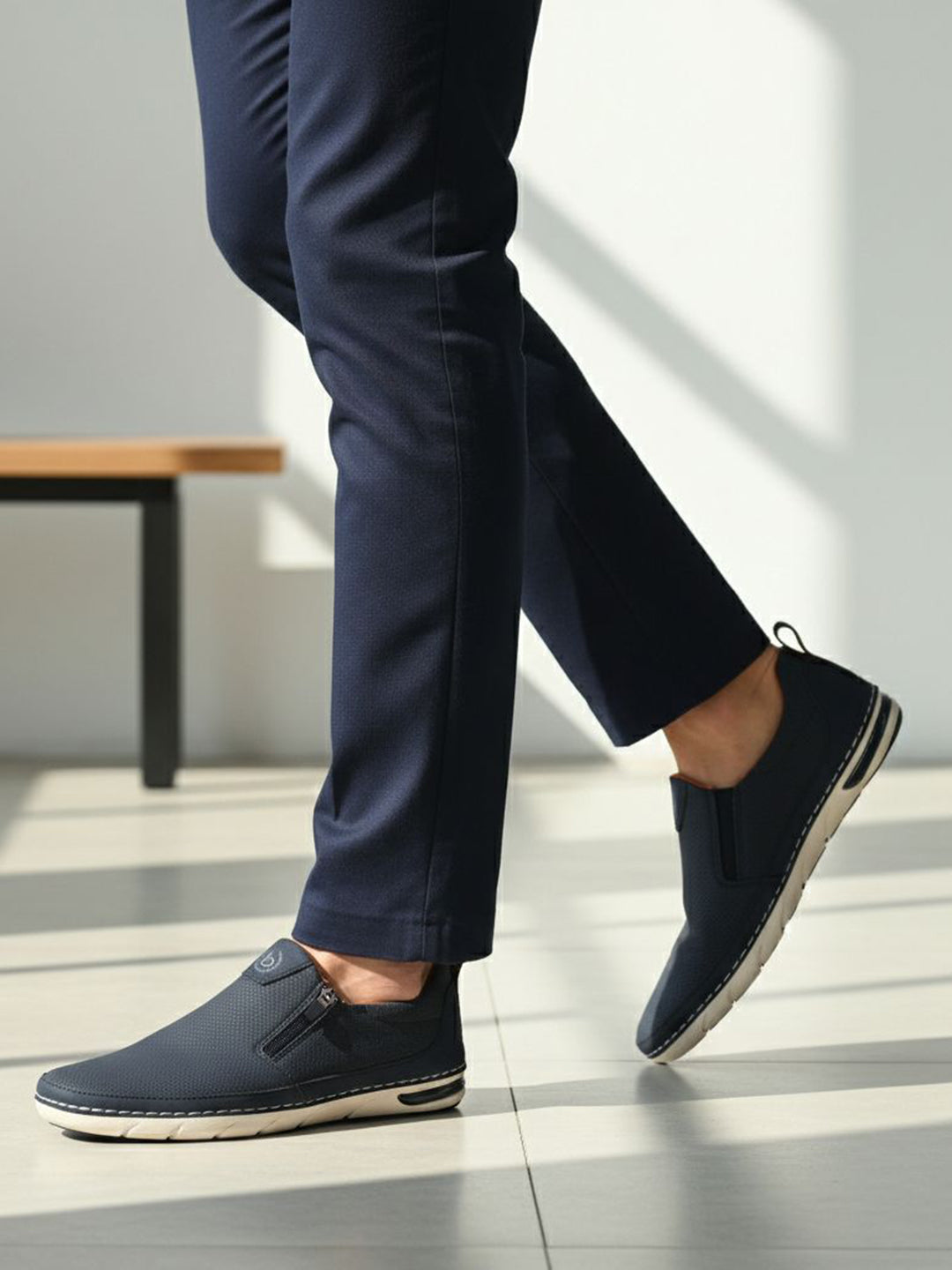 Lifestyle side view of bugatti Glenans dark blue slip-on shoes with zip detail, paired with dress pants.

