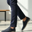 Lifestyle side view of bugatti Glenans dark blue slip-on shoes with zip detail, paired with dress pants.
