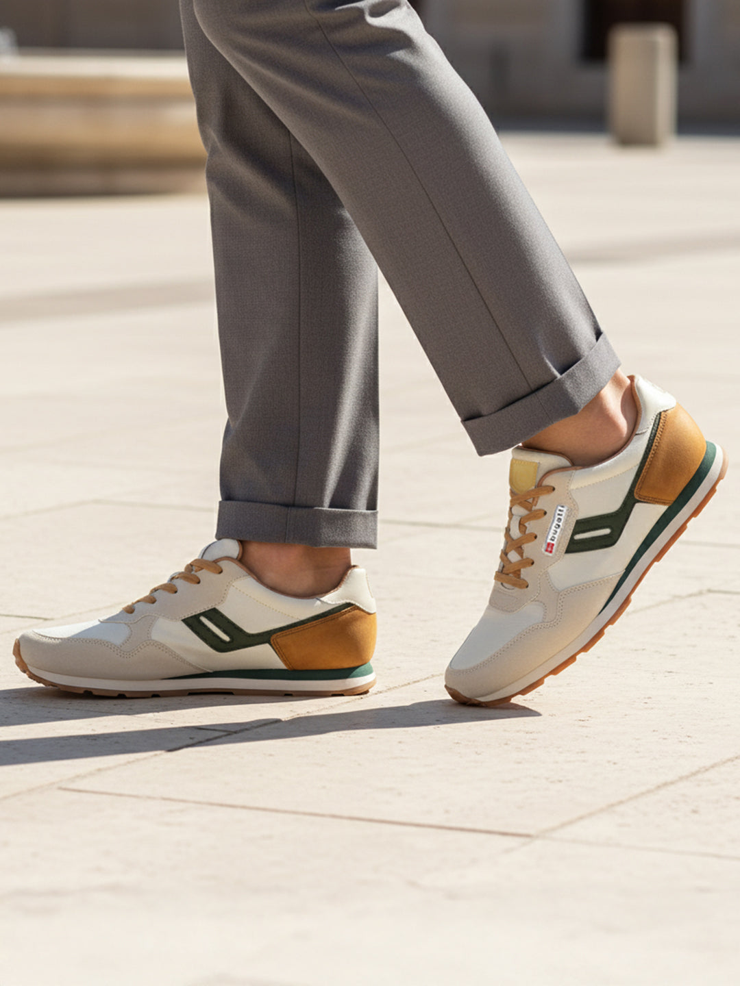 Lifestyle image of bugatti Sacramento offwhite comfort sneakers with green accents, brown heel, paired with gray dress pants.