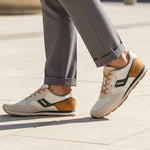 Lifestyle image of bugatti Sacramento offwhite comfort sneakers with green accents, brown heel, paired with gray dress pants.