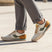 Lifestyle image of bugatti Sacramento offwhite comfort sneakers with green accents, brown heel, paired with gray dress pants.