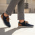 Lifestyle image of bugatti Sacramento dark blue sneakers with brown accents and laces, worn with cuffed grey trousers.
