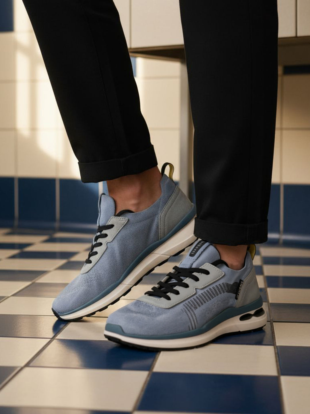 bugatti Sandar blue athleisure sneakers with black laces and white soles, paired with black cuffed pants.
