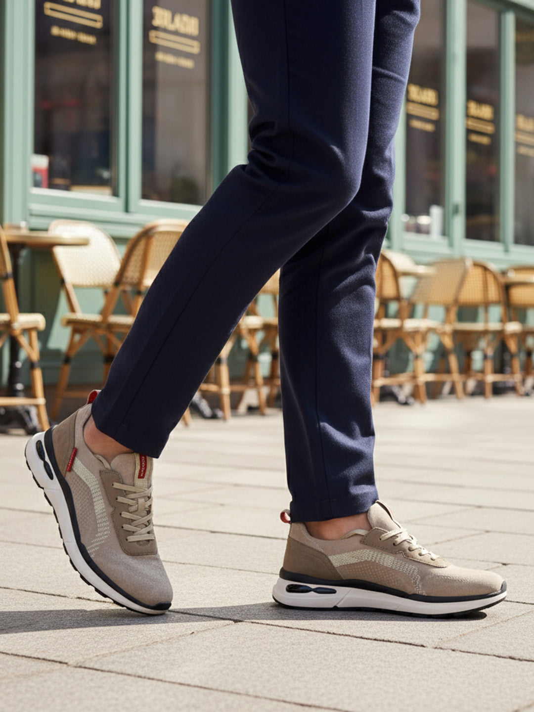 Lifestyle cropped shot of bugatti Sandar beige athleisure sneakers, with white soles, worn with dark trousers.

