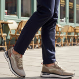 Lifestyle cropped shot of bugatti Sandar beige athleisure sneakers, with white soles, worn with dark trousers.
