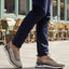 Lifestyle cropped shot of bugatti Sandar beige athleisure sneakers, with white soles, worn with dark trousers.
