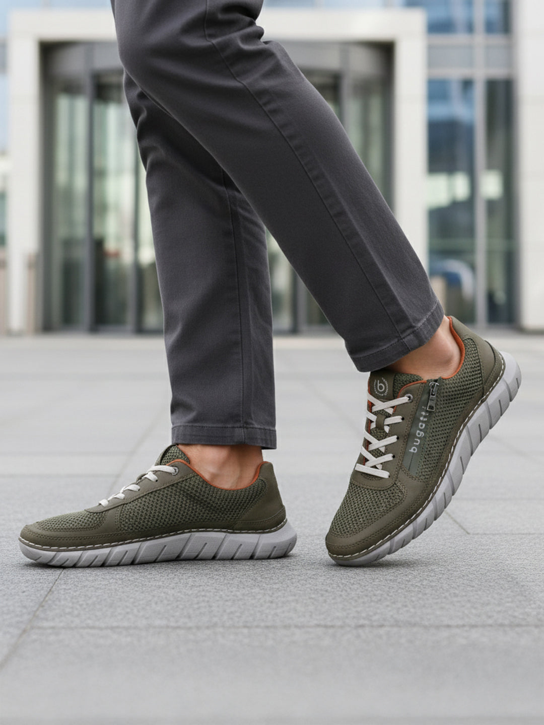 Cropped lifestyle view of bugatti Compton comfort sneakers in green, featuring a breathable mesh upper and white laces, worn with gray pants.
