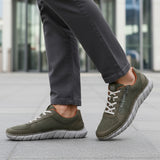 Cropped lifestyle view of bugatti Compton comfort sneakers in green, featuring a breathable mesh upper and white laces, worn with gray pants.
