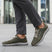 Cropped lifestyle view of bugatti Compton comfort sneakers in green, featuring a breathable mesh upper and white laces, worn with gray pants.
