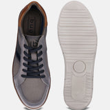 Grey low top sneakers by bugatti featuring navy laces and striped accent, next to the shoe's textured white sole.
