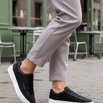 Lifestyle shot of bugatti Gunter black sneakers with a white sole, worn with grey pants.
