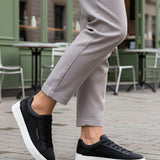 Lifestyle shot of bugatti Gunter black sneakers with a white sole, worn with grey pants.
