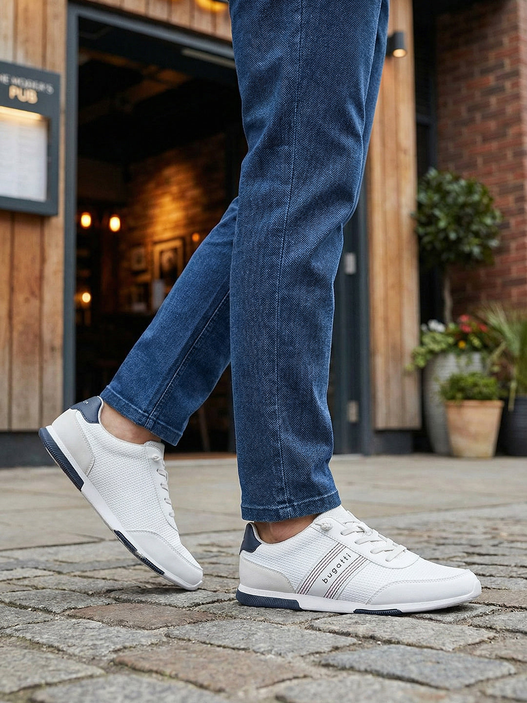 Lifestyle shot of white Bugatti sneakers with striped detail worn with blue jeans.